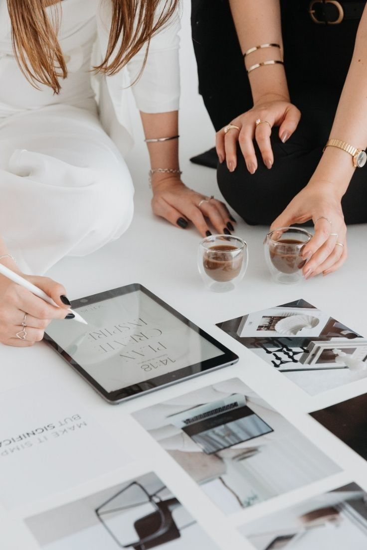 Two creatives collaborating on a white floor with print layouts and a tablet